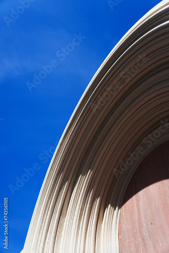 Wall decoration consist of many arch line.Sand spray texture and many size.Overlapping.Solid part is red granite stone .Background blue sky.