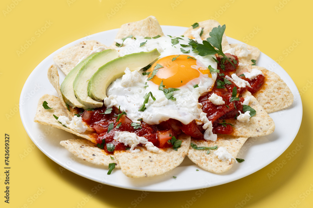 Traditional Mexican breakfast red chilaquiles with egg on yellow background