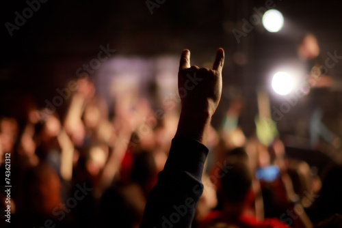 A fan's hand with devil horns protrudes from the crowd in front of the stage at a powerful metal concert. Energy and the atmosphere of a live performance. 
