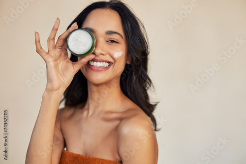 Hispanic woman holding beauty cream jar while smiling