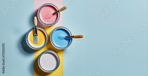 Banner with four open cans of paint with brushes on them on bright symmetry background. Yellow, white, pink, blue colors of paint. Top view. Concept of repair, hobby, art and free time. Bright colors photo