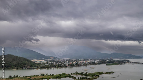 Moody panorama of a sprawling town by a river with surrounding mountains  under a dramatic overcast sky  with ample space for text  perfect for environmental or travel-themed content  Earth day concep
