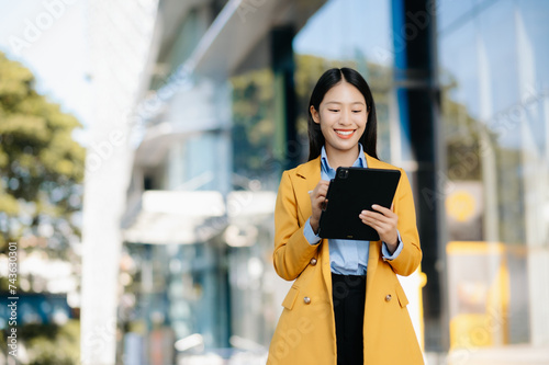 Young Asian business woman leader entrepreneur, professional manager holding digital tablet computer uon the street in big city photo