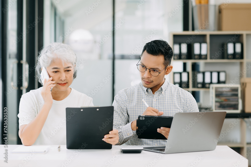 Two Asian business workers talking on the smartphone and using laptop at the office. Two Asian business workers talking on the smartphone and using laptop at the office.