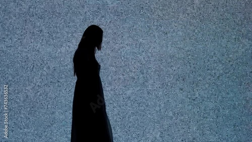 Silhouette against digital television screen. Thriller scene woman walks past big digital screen with noise comes closer to the camera looking intimidating.