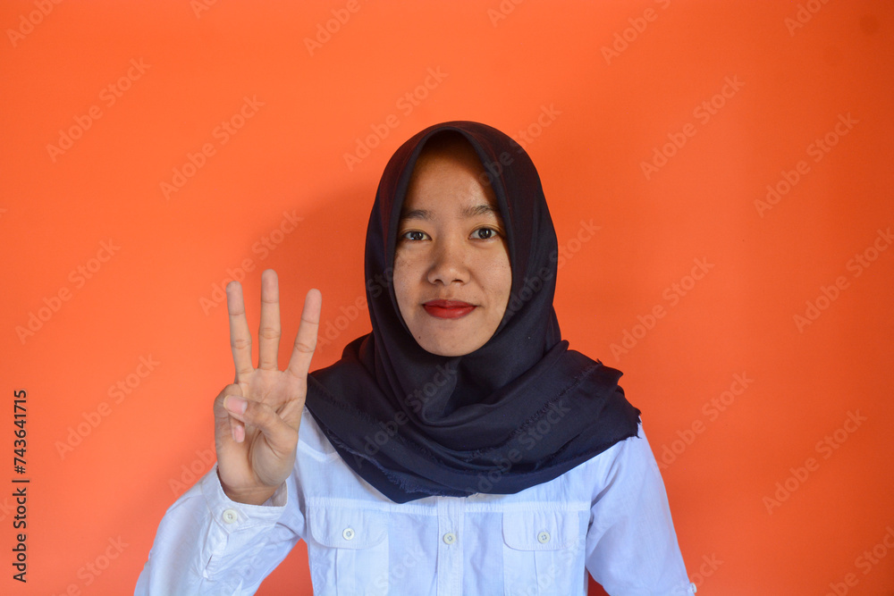Asian Muslim woman raises her fingers to form the number three. Wearing a white shirt and black hijab while smiling Asian Muslim woman raises her fingers to form the number three. Wearing a white shirt and black hijab while smiling