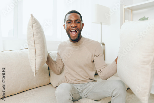 A Relaxed African American Man Sitting on a Comfortable Sofa in His Modern Living Room, Smiling and Holding a Pillow