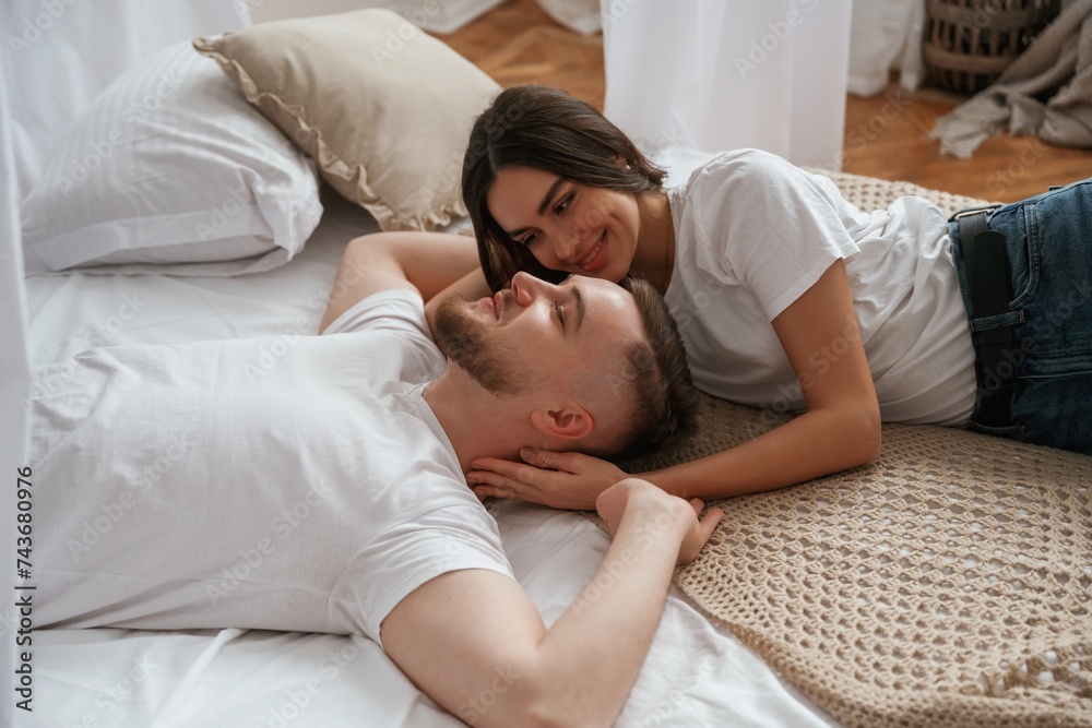 On the bed, lying down and smiling. Young couple are together at home On the bed, lying down and smiling. Young couple are together at home