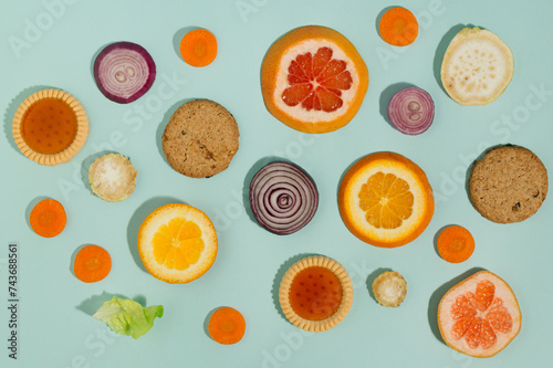 Pattern made of fruits, vegetable and biscuits. Rings of orange, grapefruit, red onion, carrot, celery. Flat lay on blue background.