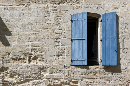 Stone facade in Beaucaire, Provence, Gard, with blue shutters half closed.