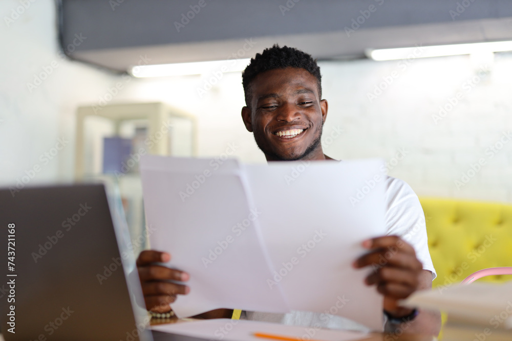 An African American businessman sits at his desk, smiling as he reads through paperwork, embodying professionalism and dedication in his work. An African American businessman sits at his desk, smiling as he reads through paperwork, embodying professionalism and dedication in his work.