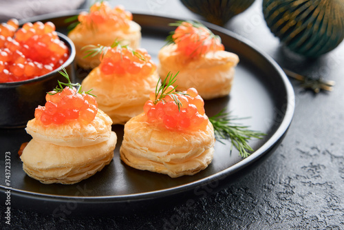 Salmon red caviar toast. Christmas canape or toast with red caviar on black plate on dark background. Idea to xmas snack. Gourmet food. Texture of caviar. Seafood.