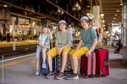 Children, boy brothers holding suitcases, travelin, waiting at trainstation to go to the airport