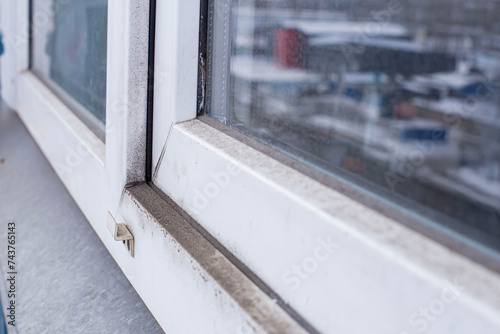 A woman in a rubber glove points to the mold. Plastic window and window sill in mold and dirt. Fungus and dampness at the wet window. Space for text. Shallow depth of field.
