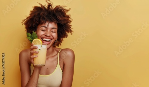 Portrait of happy young African american woman in bright summer outfit drinking refreshing cocktail isolated on yellow background