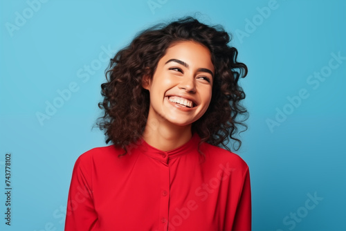 Happy woman in red dress in front of plain blue background © Stephen