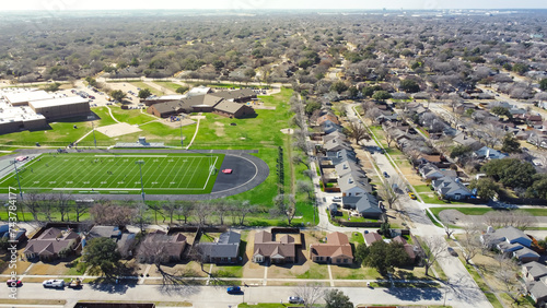 Residential neighborhood and school district with row of single family homes, football stadium artificial turf, yard markings, track and field, subdivision urban sprawl in Dallas, Texas, USA