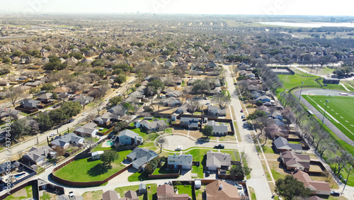 Aerial view upscale residential neighborhood with downtown skyline in distance background, single family houses with large backyard, swimming pool, wooden fence near school football field, Dallas