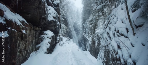 A person is skiing down a snowy path in the wintery surroundings of the Flume Gorge trail in Franconia Notch State Park, New Hampshire. The skier is navigating the curvy path with skill and speed. photo