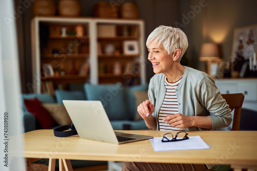 A satisfied senior adult woman having a video call online meeting on a laptop while working from home