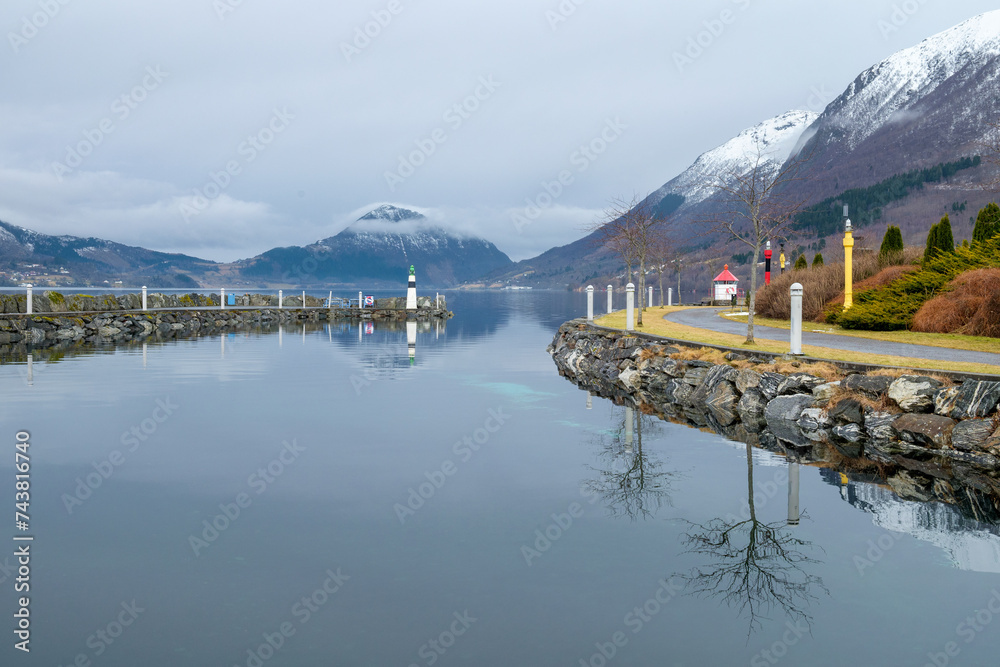 Serene fjord landscape with snowy peaks reflected in still water, during a calm winter morning.
