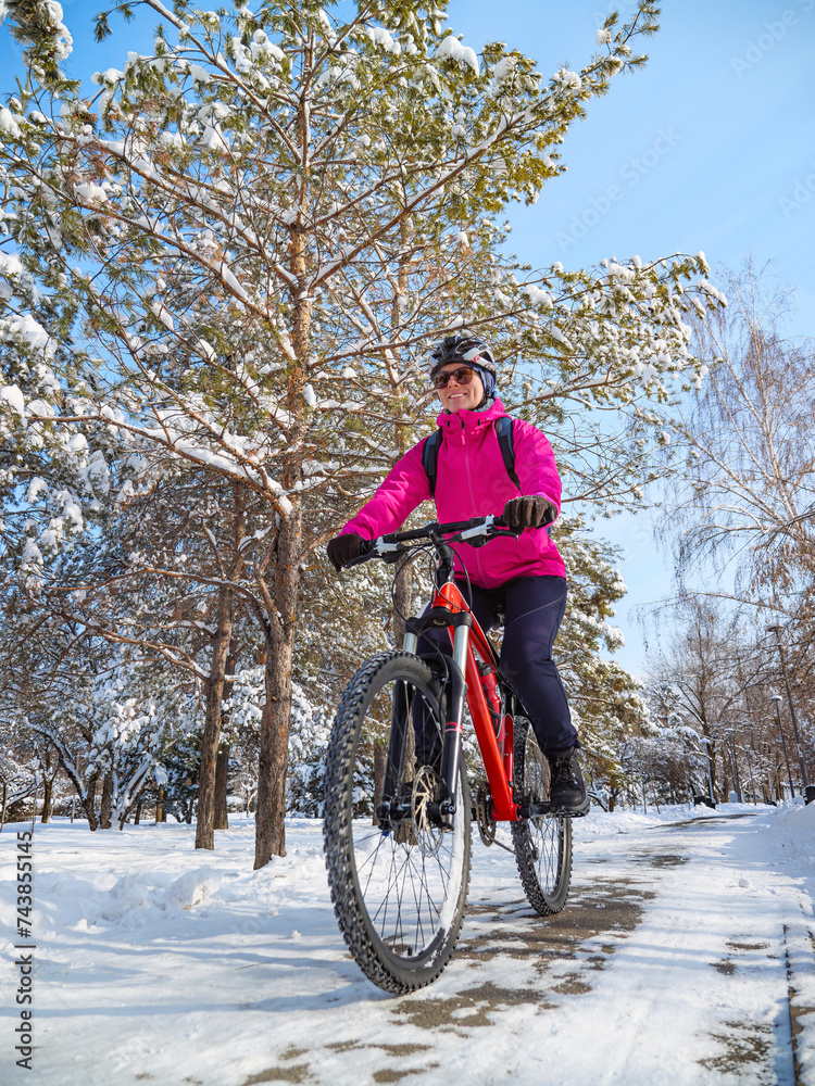 Winter cycling adventure. A girl in a pink jacket among snow-covered trees rides a bicycle along a path in the park Winter cycling adventure. A girl in a pink jacket among snow-covered trees rides a bicycle along a path in the park