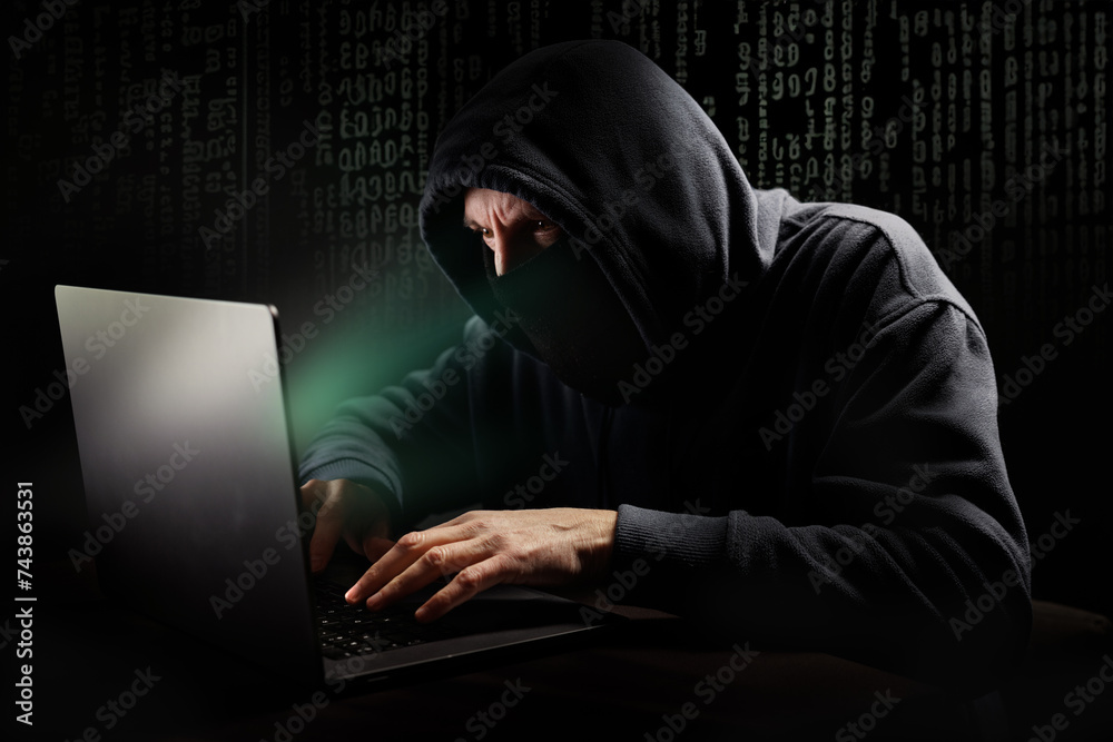 Pirate informatique masqué en train de pirater un ordinateur portable et qui demande une rançon devant un écran vert Pirate informatique masqué en train de pirater un ordinateur portable et qui demande une rançon devant un écran vert
