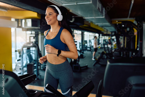Happy female athlete running on treadmill while exercising in health club.