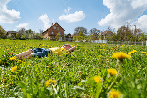 Boy lies on grass in dandelions flower filed looking to the sky. Outdoor . Side view. photo