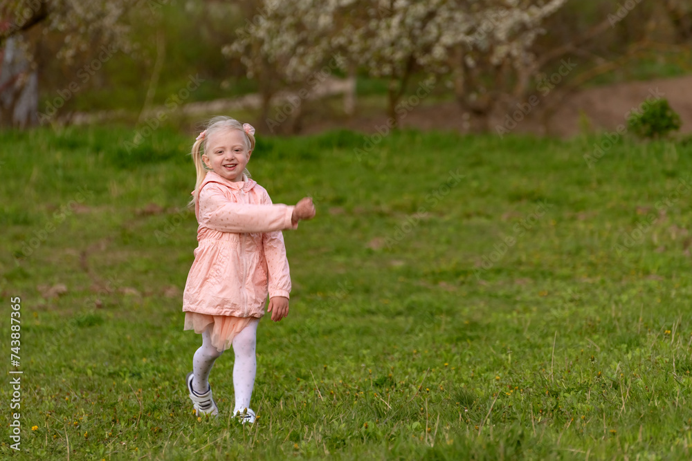 Portrait of little girl in pink outfit walking in green meadow. Child walks through clearing in spring park. Portrait of little girl in pink outfit walking in green meadow. Child walks through clearing in spring park.