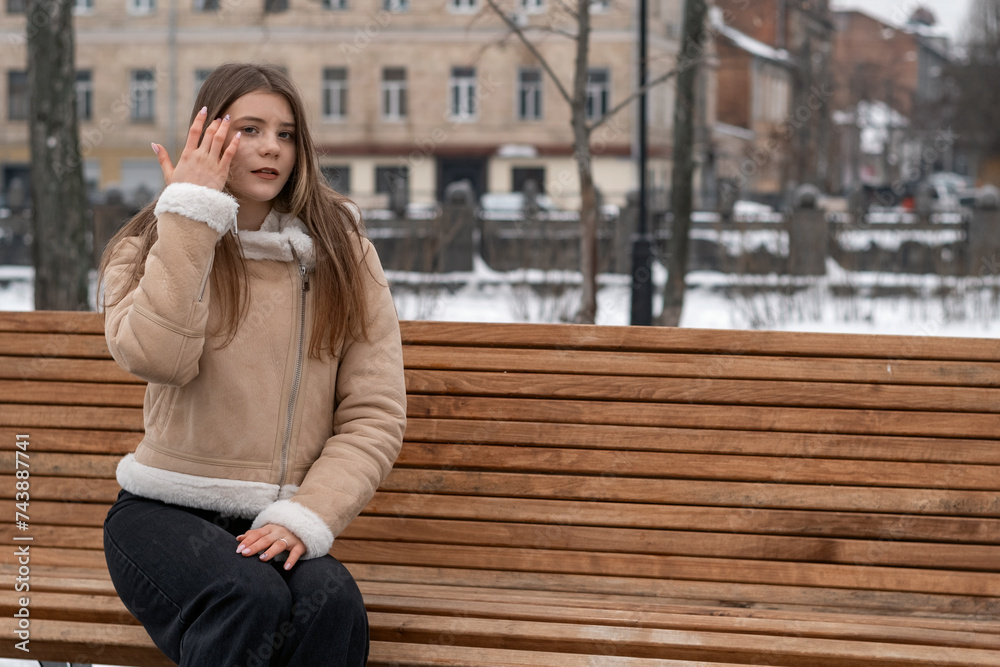 Fototapeta premium Young beautiful girl sitting on a bench in the city in winter.