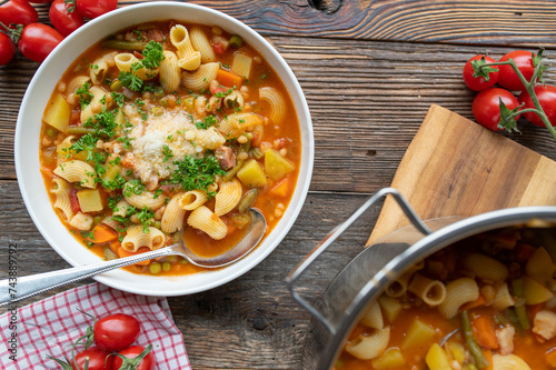 Italian minestrone with vegetables, beans, pasta and parmesan cheese on a plate on wooden table background photo