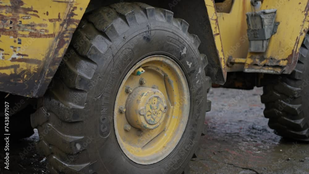 A yellow bulldozer with large wheels on a dirt road next to a pile of cars. The vehicles tires show worn tread from being submerged in water A yellow bulldozer with large wheels on a dirt road next to a pile of cars. The vehicles tires show worn tread from being submerged in water