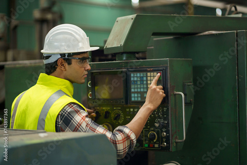 indian industrial worker beard man with helmet controlling cnc machine or maintenance in industry factory . labor male asian india Engineer standing repairing and fixing monitor in manufacturing.