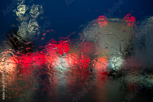 This image shows a dazzling abstract view of street lights and vehicle headlights diffused through a rain-drenched car windshield at night. The rain creates a dynamic, fluid texture on the glass © Bjorn B