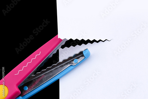 Pinking shears cutting a white piece of paper.