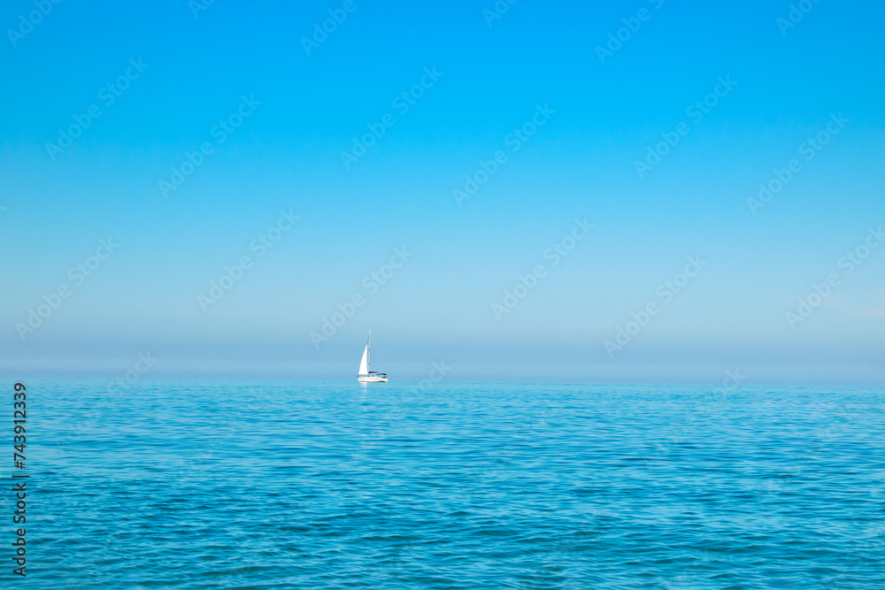 Obraz premium white sailboat on the open sea near the horizon against a cloudless sky. Boat trip. place for text