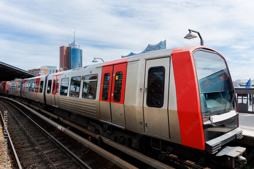 Hamburg Red Unmanned U-bahn Subway train on Baumwall station on Elevated Track with Hamburger Port Harbor Elbphilharmonie building background blue sky. Hanseatic city commute transport scenic view Hamburg Red Unmanned U-bahn Subway train on Baumwall station on Elevated Track with Hamburger Port Harbor Elbphilharmonie building background blue sky. Hanseatic city commute transport scenic view