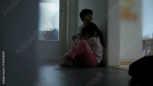 Family Bond During Difficult Times - Brother Comforting Sister, Childhood Depression and Sympathy Concept seated in gloomy corridor