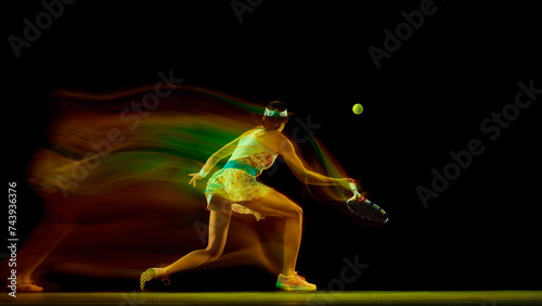 Dynamic photo of young woman preparing to hitting ball against black studio background in motion blur. Fast movement Concept of sport, active lifestyles, tournaments, competition, energy. Ad © Lustre