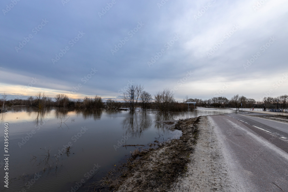 early spring flood, river overflowing its banks, trees in the water, flooded road, environmental pollution, ecology