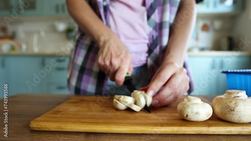 A woman prepares food in the kitchen at home. Slices mushrooms with a knife on a cutting board photo