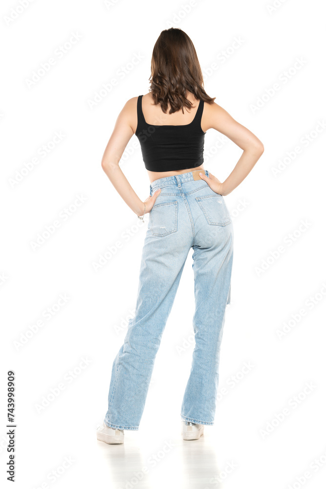 Young female model wearing ripped jeans and black sleeveless shirt posing on a white background. Back, rear view Young female model wearing ripped jeans and black sleeveless shirt posing on a white background. Back, rear view