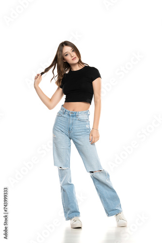 Young female model wearing ripped jeans and black shirt posing on a white studio background. Front view