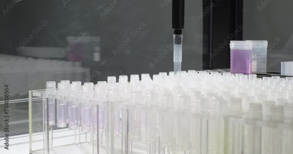 Robotic arm pours purple liquid into test tubes. Scientific laboratory of biotechnology, chemistry, biochemistry and scientific experiment. Vaccines and medicines development. Close-up Robotic arm pours purple liquid into test tubes. Scientific laboratory of biotechnology, chemistry, biochemistry and scientific experiment. Vaccines and medicines development. Close-up