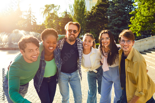 Portrait photo of multinational company of happy friends on walk on sunny summer day in city park. Attractive young people look into camera and smile. Concept of youth lifestyle and friendship. photo