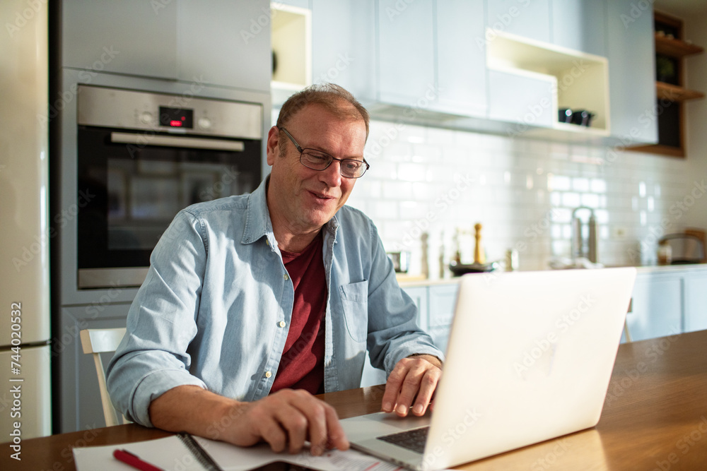 Smiling middle aged man using laptop at home Smiling middle aged man using laptop at home