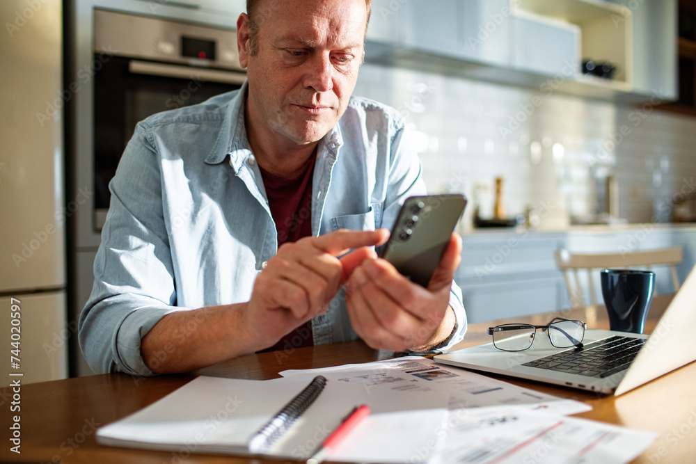 Close-up of a man using a smartphone with a laptop and documents on the table