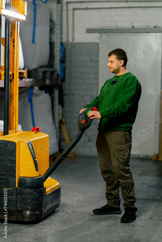 A worker at coffee factory uses a yellow lifting fork to lift and insert forks into pallets