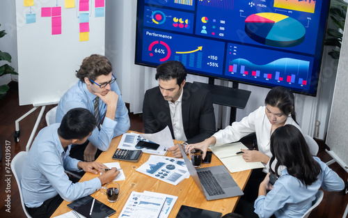 Wide top view of diverse group of business analyst team analyzing financial data report paper on meeting table. Chart and graph dashboard by business intelligence analysis. Meticulous